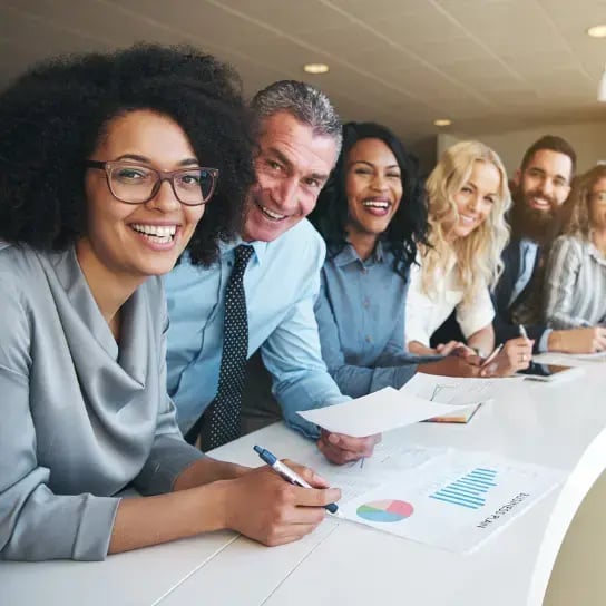 A diverse group of professionals is seated at a table, reviewing the impact of offering employees a gym membership subsidy in a modern office setting.