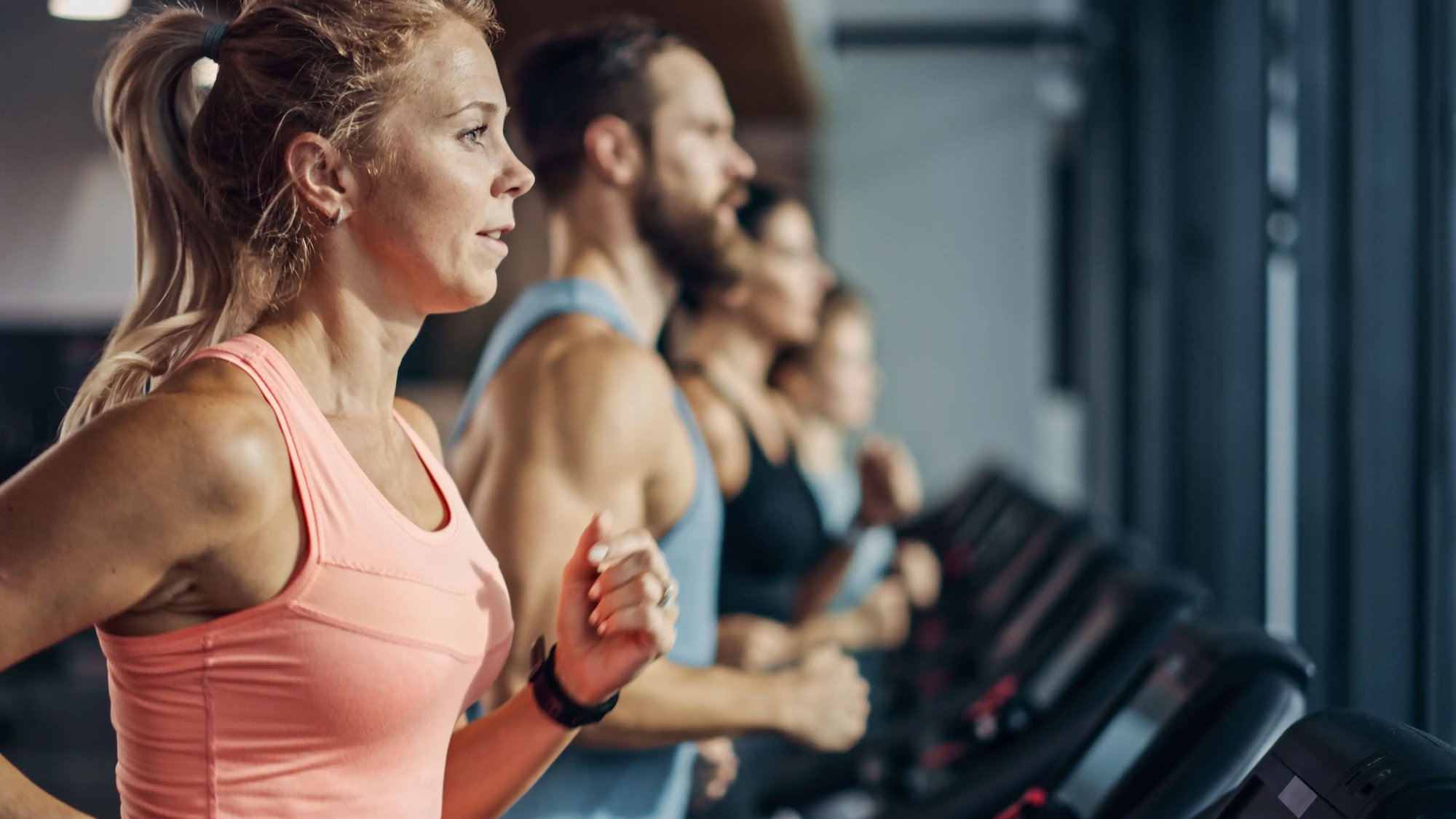 A group of people running on treadmills in a gym setting, engaged in physical fitness activities.