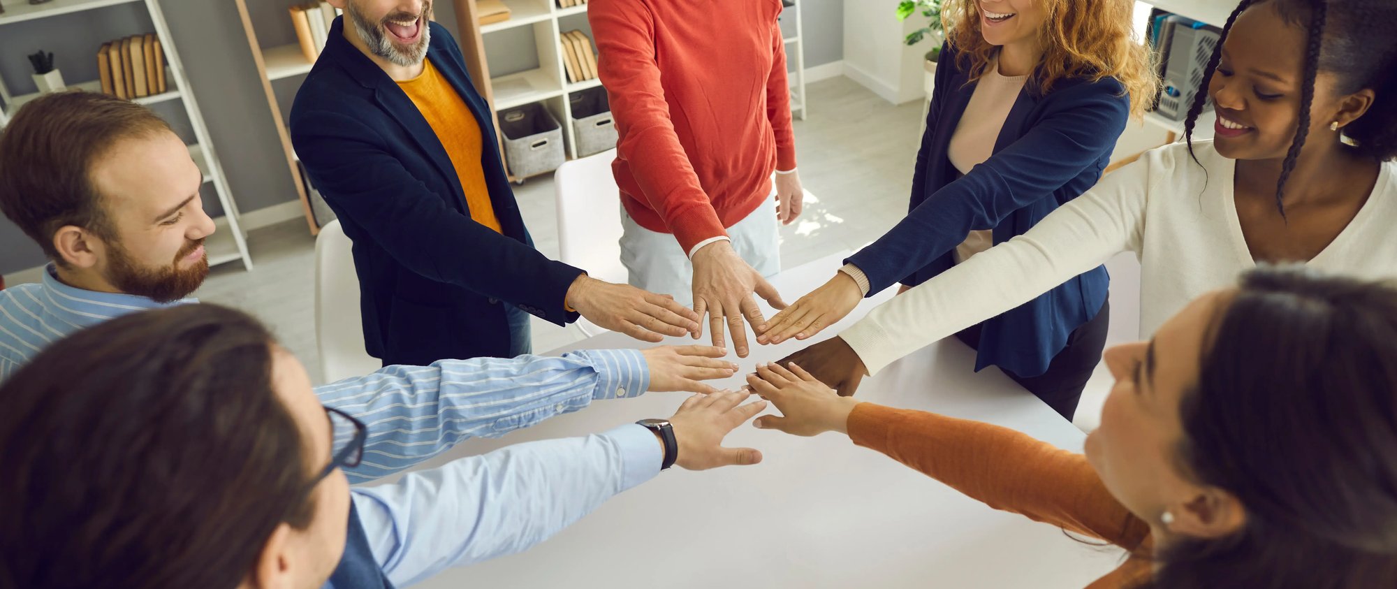 A diverse group of people standing together with their hands placed in a circle, demonstrating unity and teamwork.