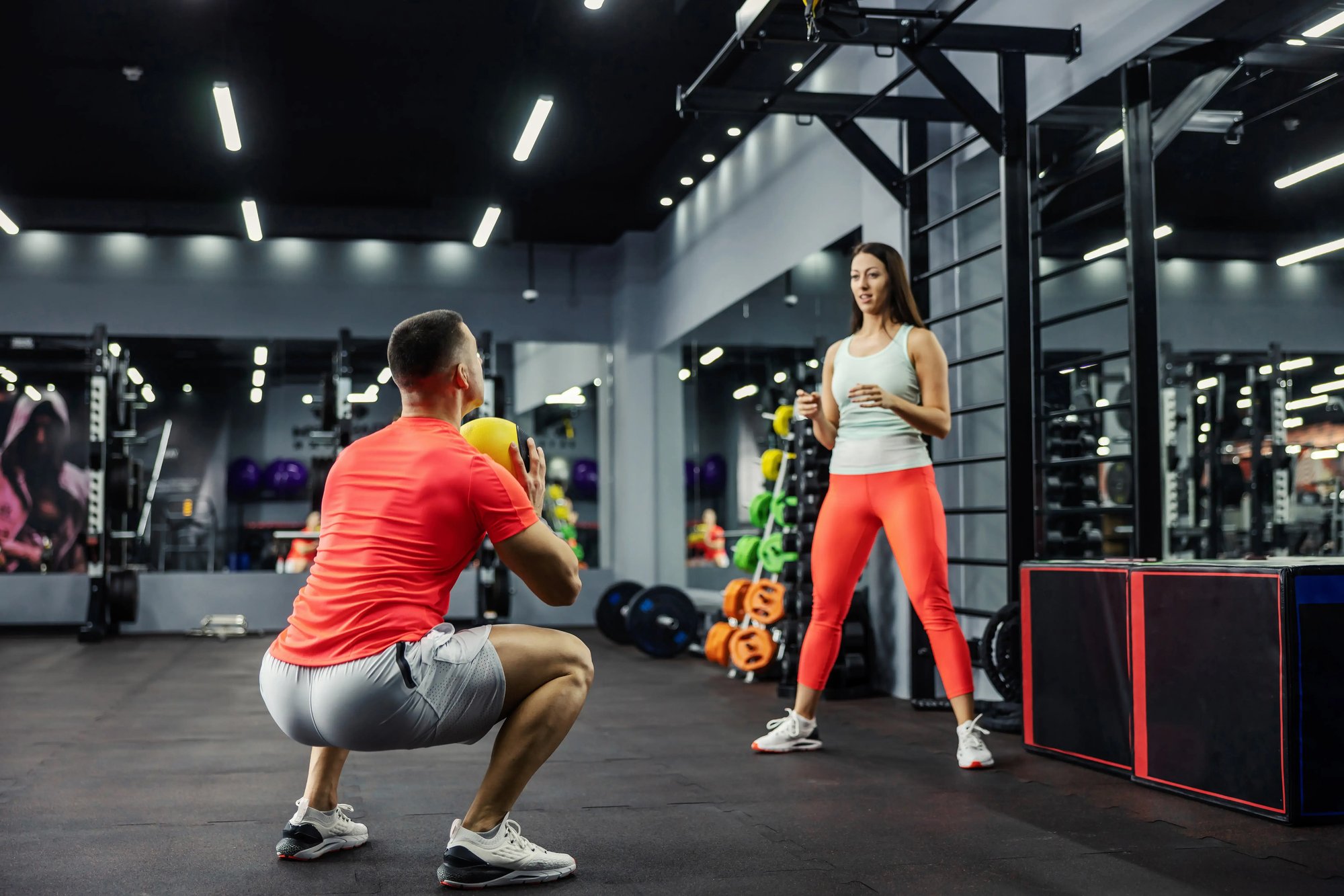A man and woman are exercising in a gym, utilising weights and exercise equipment thanks to their discounted gym memberships through Epassi UK's employee benefit schemes.