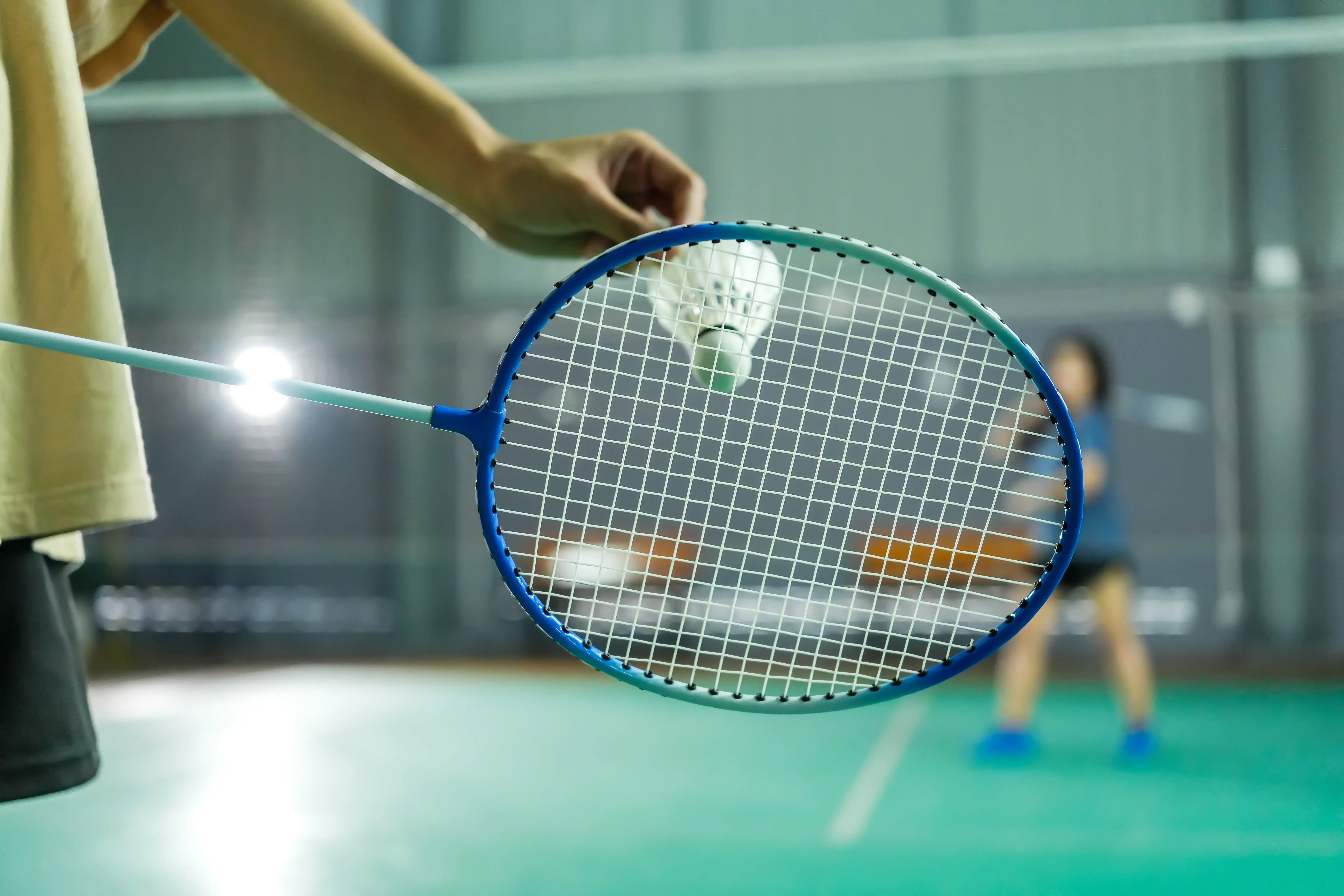 A hand gripping a racquet, about to serve on a badminton court.