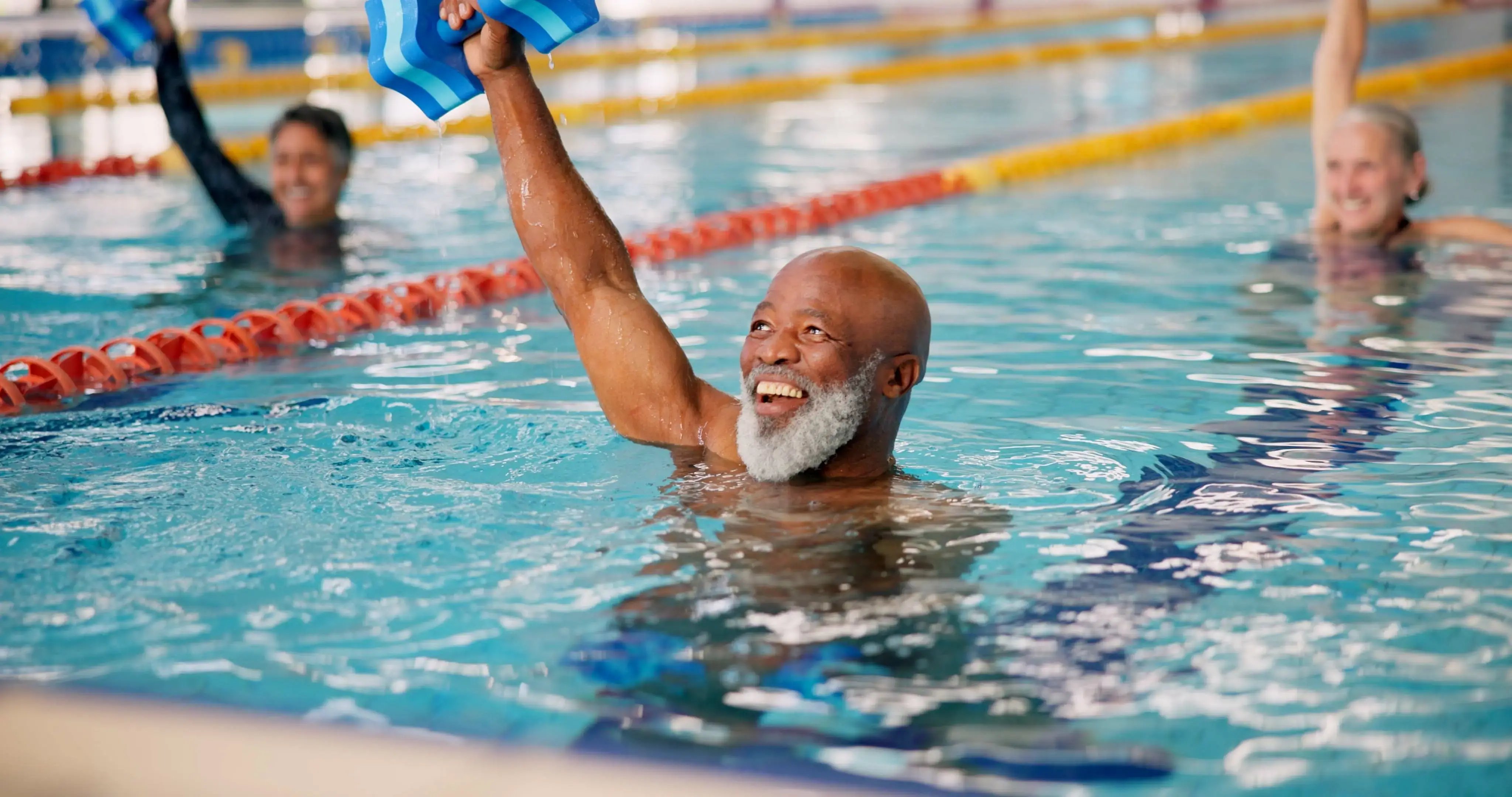 A man in a swimming pool smiling doing aerobics.