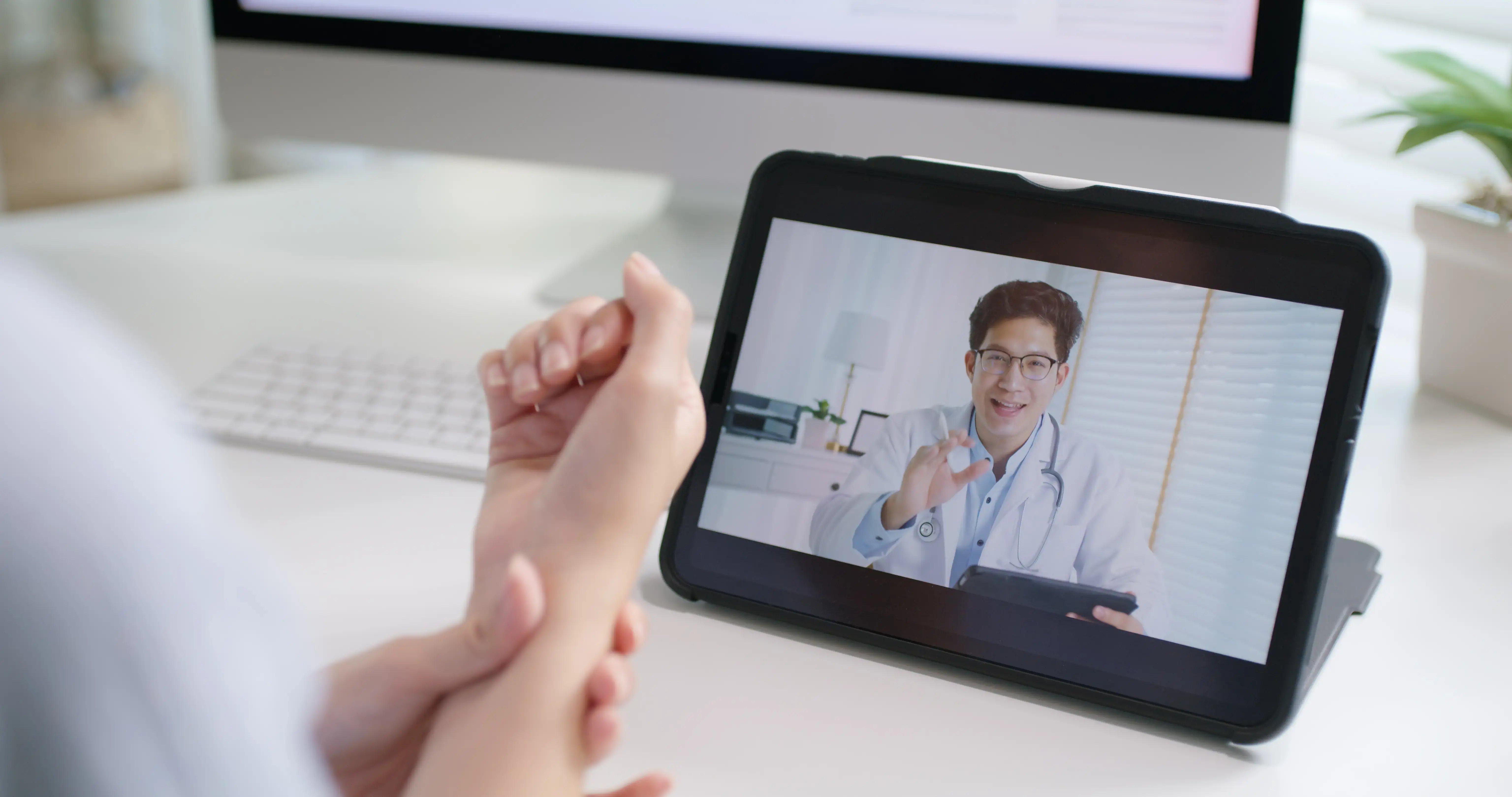 A patient holding their painful wrist positioned in front of a computer screen during a virtual physiotherapy session.