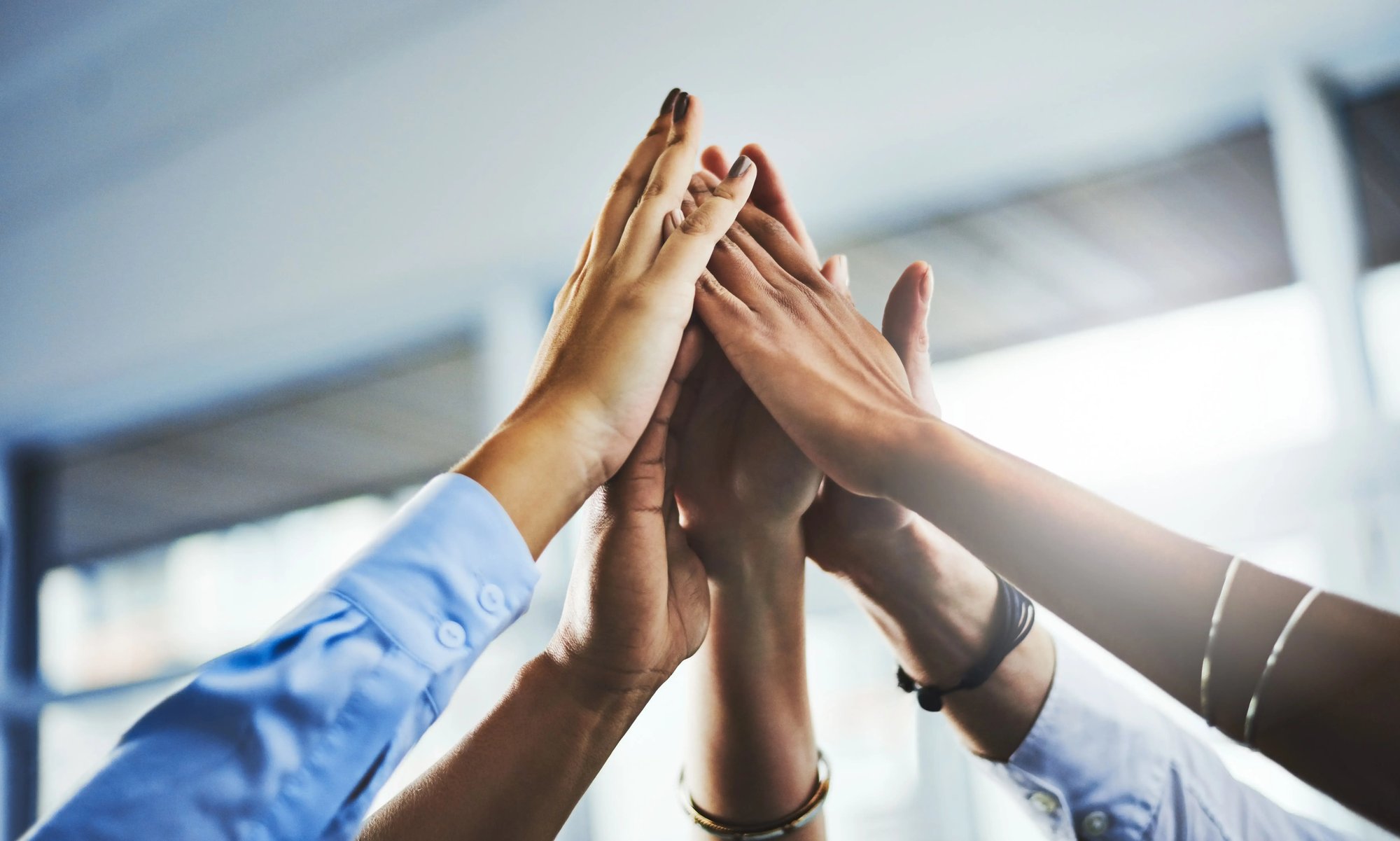 A group of team of colleagues celebrating their employee benefits with a team high-five.