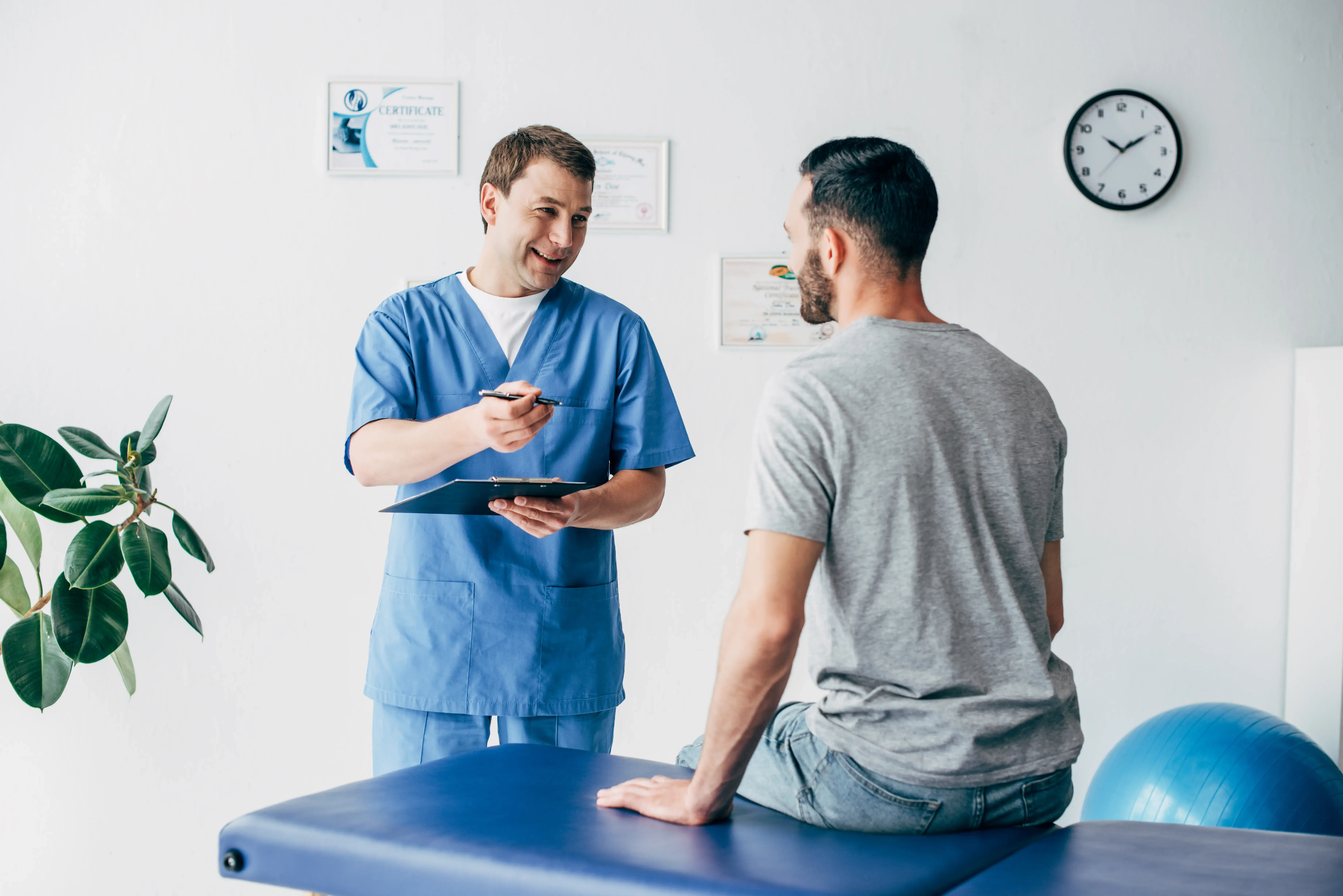 A man sitting on assessment table, engaging in conversation with a doctor during a health check.